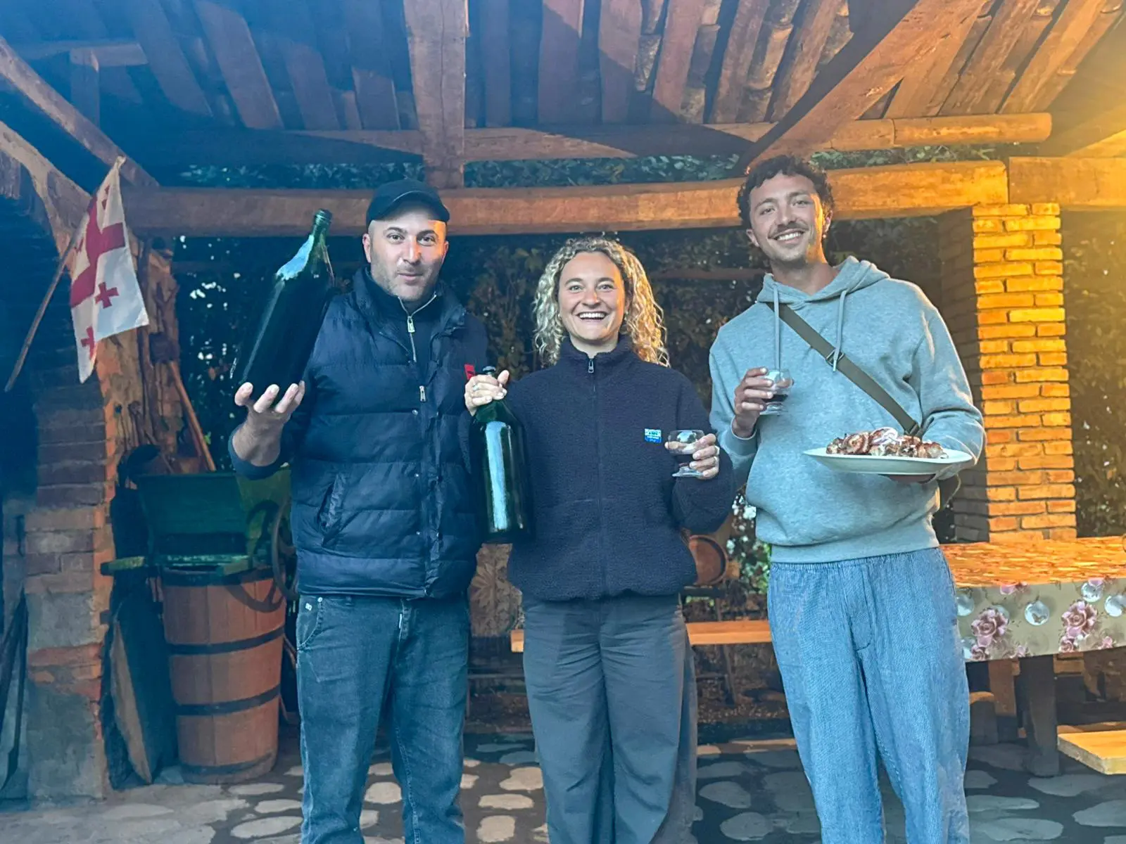 three people holding wine bottles and food in Georgia