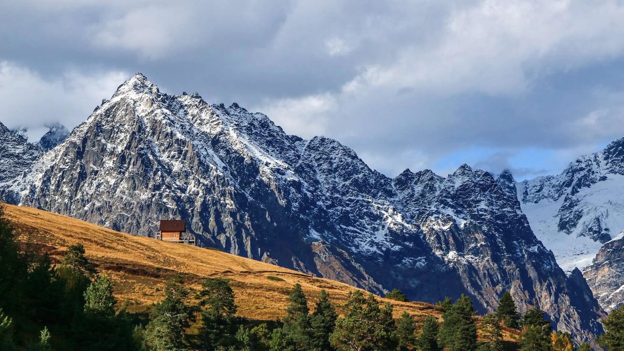 Houten hut op een gouden heuvel met besneeuwde bergen in Georgië